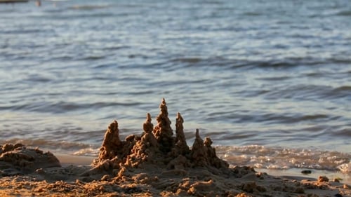 A Small Sandcastle On Beach With Waves On The