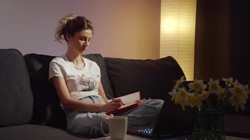 Woman Writing in Notebook on Couch at Home