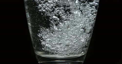 Wasser wird vor schwarzem Hintergrund in Glas gegossen, Zeitlupe 4K