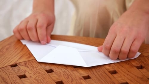 Hands Folding White Paper on Wooden Table
