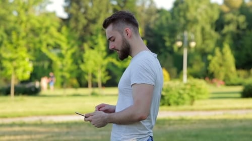Young Man Walking In The Park With Mobile Phone