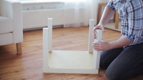 Man Assembles a Small White Table Indoors