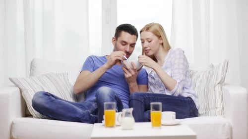 Cheerful Couple Eating Cereal Together on Sofa