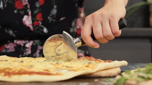 Cutting Pizza with Pizza Cutter in Kitchen