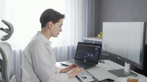 Schöne junge Frau lächelt in die Kamera, während sie an ihren beiden Computern arbeitet