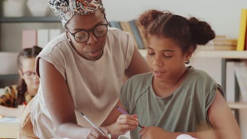Afro-American Female Teacher Helping Girl during Lesson in Elementary School