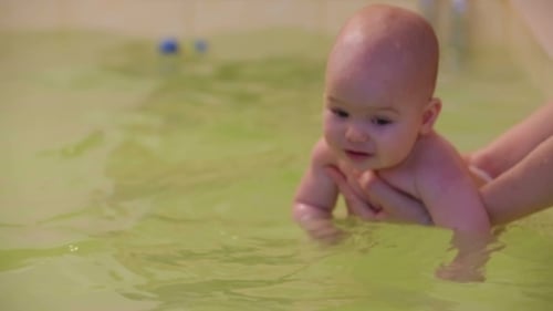 Infant Swimming in Green Water with Caregiver
