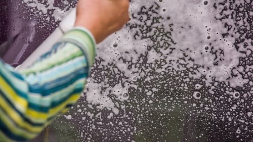 Human Hand Spraying Washing Foam On House Window