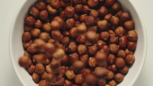 Hazelnuts Falling Into A White Bowl
