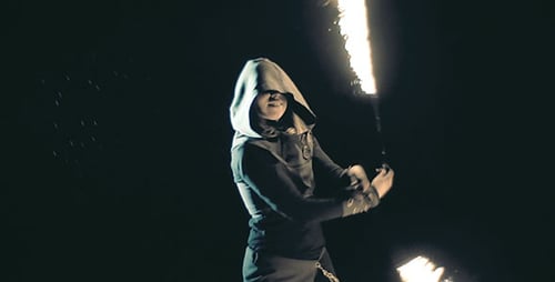 Hooded Figure Jugging Fire Sticks in Dark Setting