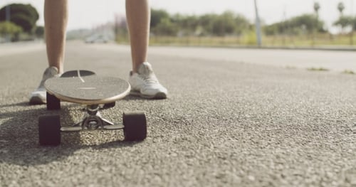 Young Adult Standing with Skateboard on Road