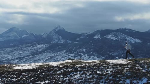 Aerial View of a Running Man Against the Backdrop of a Mountain Landscape in Winter