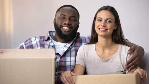 Glückliches Paar mit gemischter Rasse hält Kartons in der Hand, bezugsfertig in neuer Wohnung