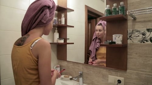 Young Woman Brushing Teeth in Bathroom Mirror