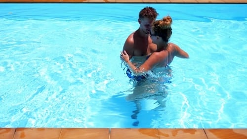 Pareja joven abrazándose en la piscina al aire libre azul