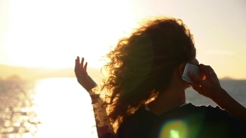 Woman Talking on Phone at Sunset by Ocean