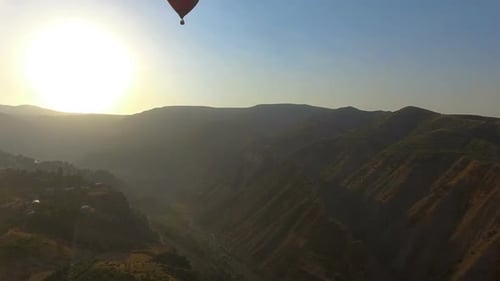 Blick auf den Heißluftballon, der über das Bergtal und das armenische Dorf fliegt, Sonnenuntergang