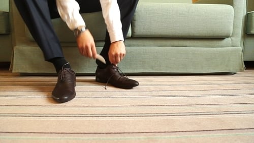 Man Tying Brown Leather Shoes on Couch