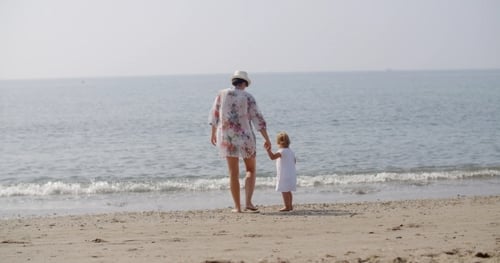 Woman Walking Hand In Hand With Child On Beach