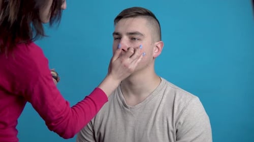 Make-up wird auf einen jungen Mann aufgetragen. Das Mädchen schminkt einen Mann, bevor es auf Blau schießt