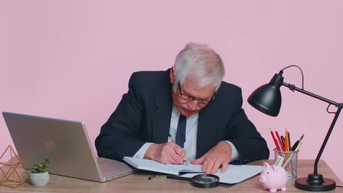 Senior Man Writing in Notebook at Desk