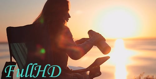 Woman Drinking in Chair Next to Ocean at Sunrise