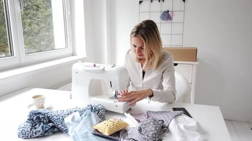 Blonde Woman Sewing at Modern Machine in Bright Room