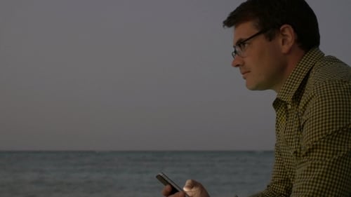 Young Man Using Smart Phone By Sea In The Evening