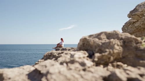 Woman Sits on Edge Cliff and Looks Into Sea