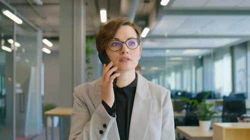 Businesswoman Going through Office and Speaking on Phone