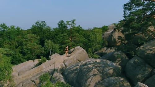 Woman Standing on Rocky Outcrop in Lush Wilderness