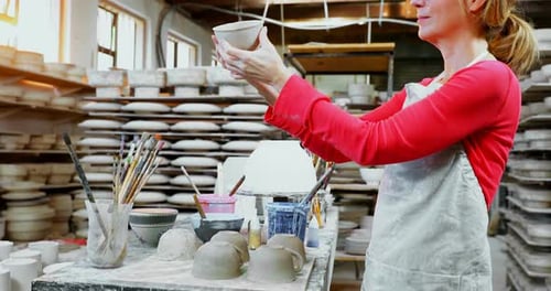 Woman Inspects Ceramic Mug in Pottery Studio