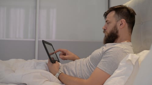Man Using Tablet in Bed Indoors