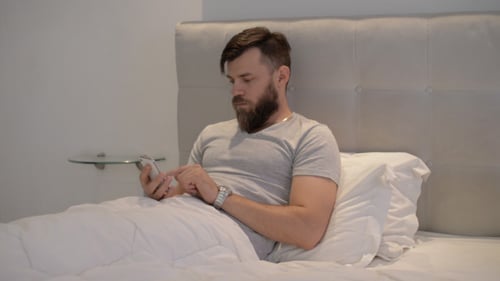 Man Relaxing in Bed Using Mobile Phone
