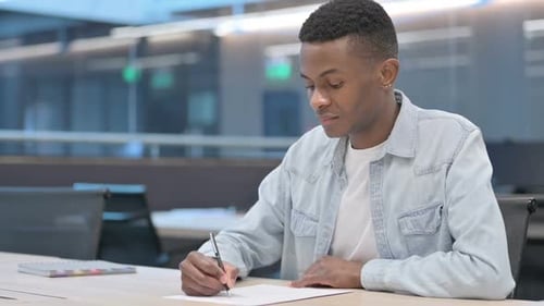 Young Adult Concentrating and Writing at Desk Indoors