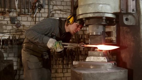 Ein Schmied formt mit einer industriellen Druckmaschine ein Messer