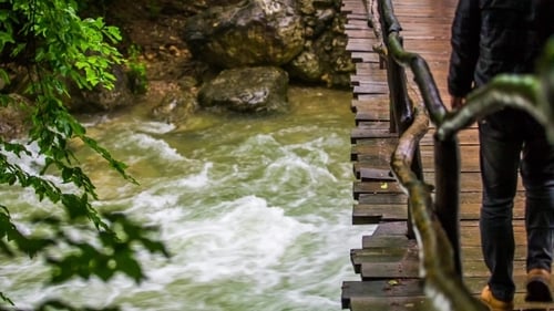 Man Walking On Bridge Hanging Above Rough River