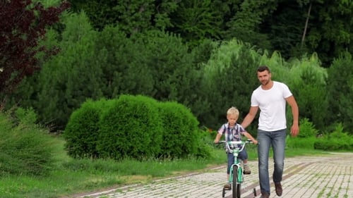 Father Teaching Son To Ride Bike In Park