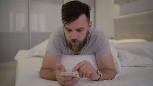 Man Lying on Bed Using Smartphone
