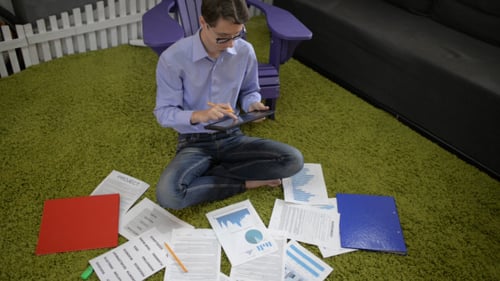 Young Adult Working on Tablet at Home Surrounded by Documents
