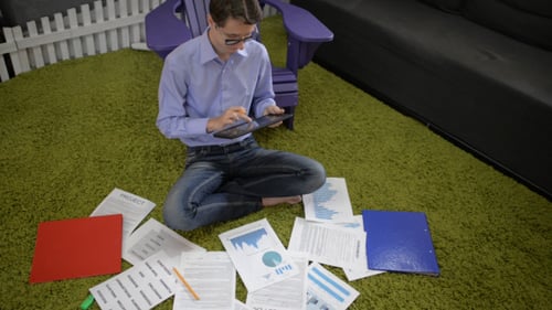 Young Adult Sitting with Business Documents Using Tablet