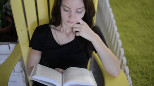 Young Woman Reads Book on Porch Outdoors