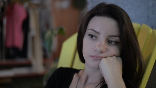 Thoughtful Woman Resting Chin on Hand in Yellow Chair
