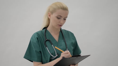 Young Woman in Scrubs Taking Notes on Clipboard