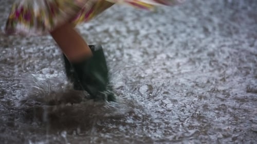 Child Jumps in Rainy Urban Puddle With Boots