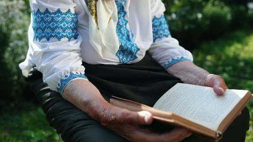 An Old Grandmother is Sitting on the Street and Reading a Book