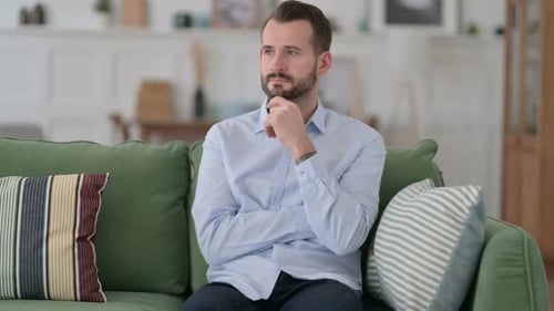 Bearded Man Ponders Thoughtfully on Green Couch