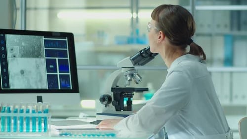 Female Scientist Using Microscope and Computer in Lab