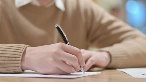 Nahaufnahme eines jungen Mannes, der auf Papier schreibt