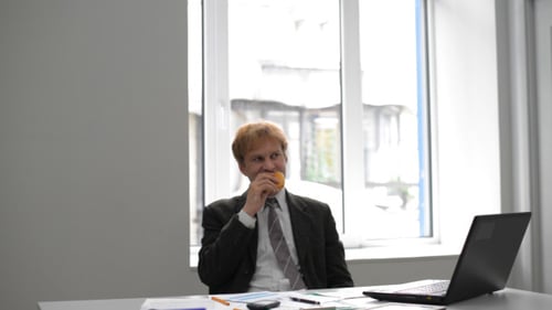 Adult Eats Pastry at Desk in Office